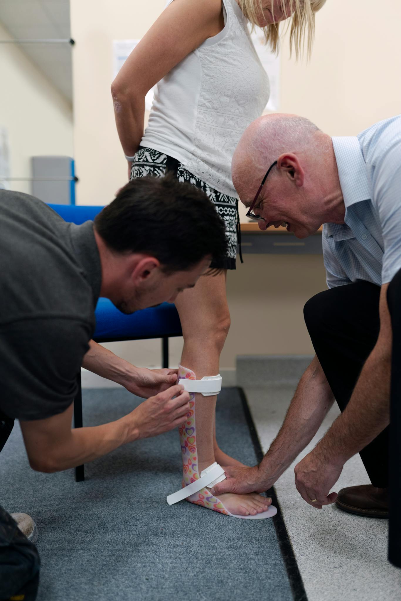 Healthcare professionals assisting a woman with an ankle brace fitting indoors.