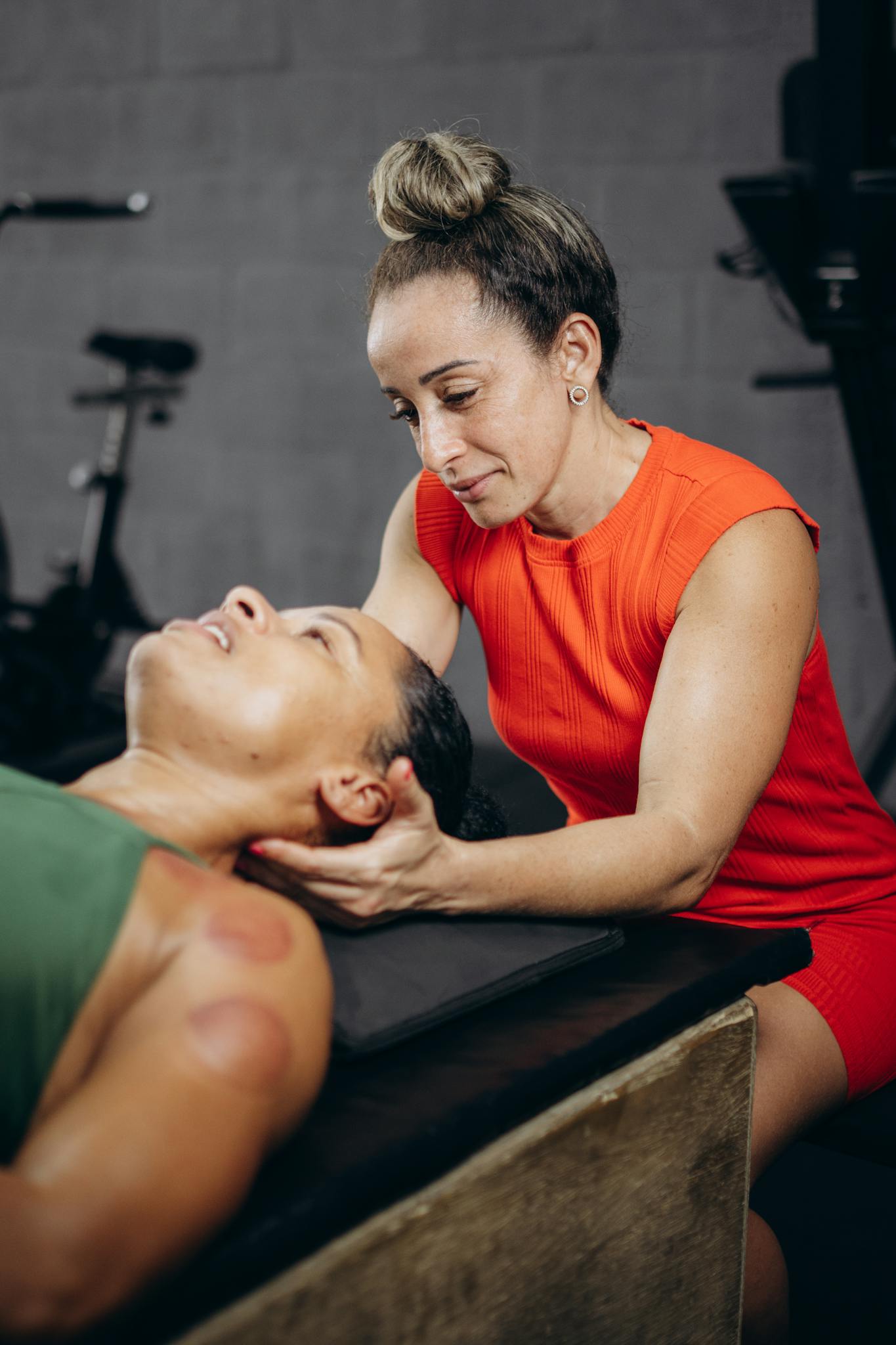 Physiotherapist assisting a client with neck treatment in a gym setting.